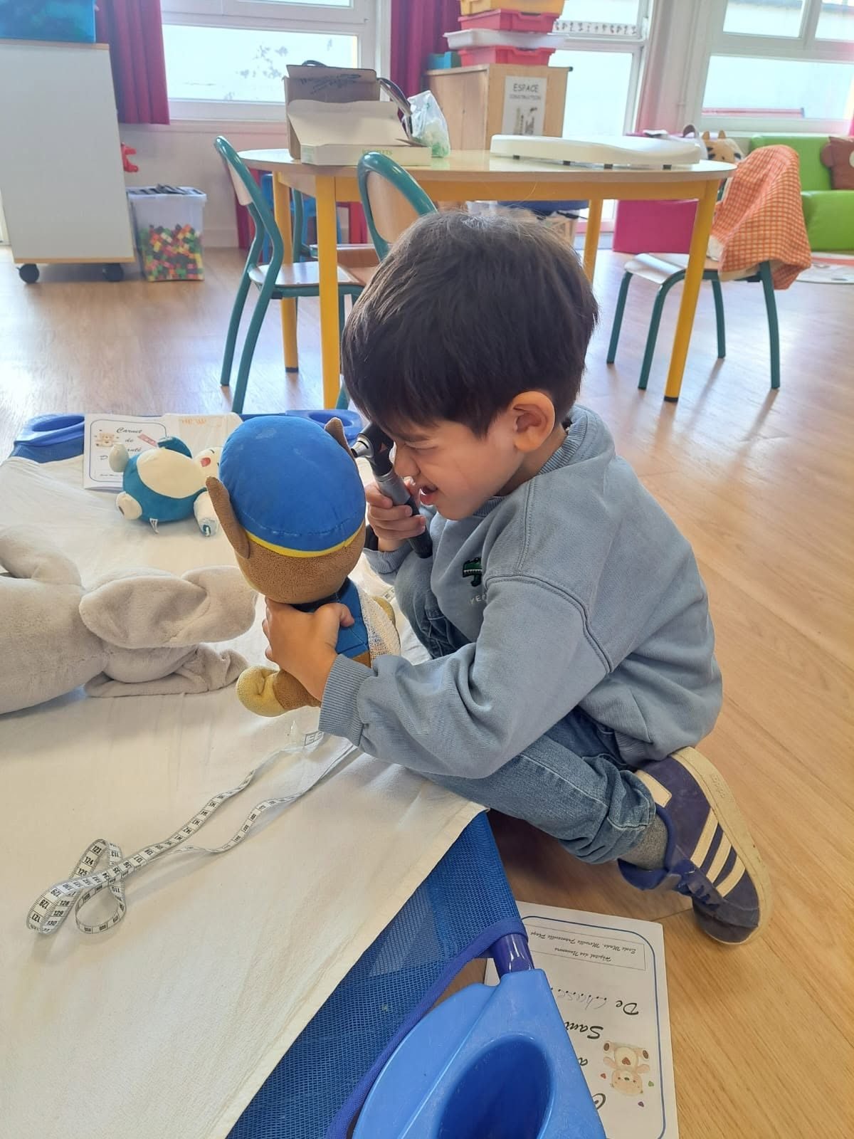 Un enfant ausculte sa peluche avec un otoscope, a cote du carnet de sante du nounours.